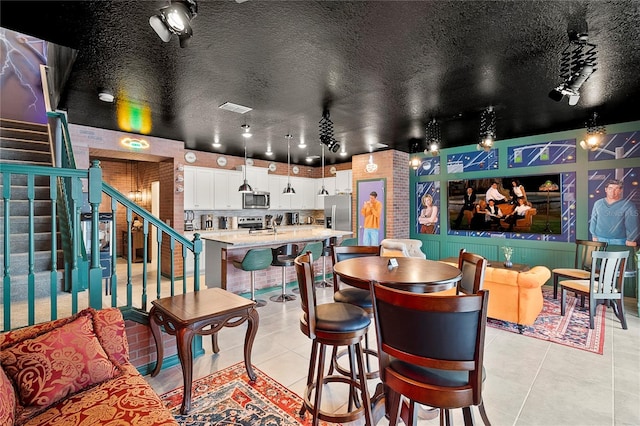 tiled dining room featuring bar area, a textured ceiling, and brick wall