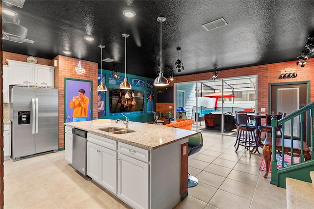 kitchen featuring a kitchen island with sink, sink, stainless steel appliances, light stone countertops, and white cabinetry