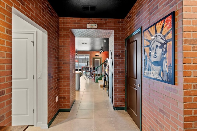 hall featuring brick wall, a textured ceiling, and light tile floors