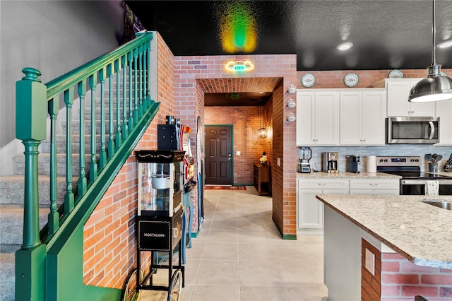 kitchen with pendant lighting, stainless steel appliances, brick wall, light stone countertops, and white cabinetry