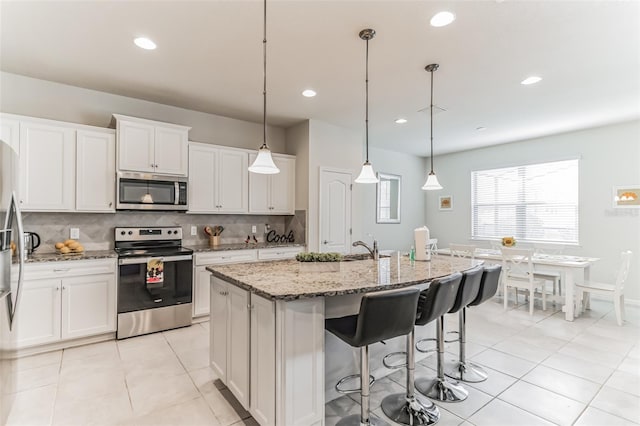 kitchen with white cabinets, appliances with stainless steel finishes, hanging light fixtures, and an island with sink