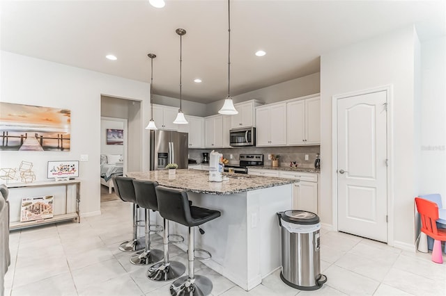 kitchen featuring light stone countertops, stainless steel appliances, backsplash, an island with sink, and white cabinets