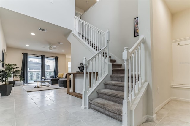 stairway with a towering ceiling, tile patterned floors, and ceiling fan