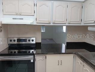 kitchen with dark countertops, electric range, range hood, and white cabinetry