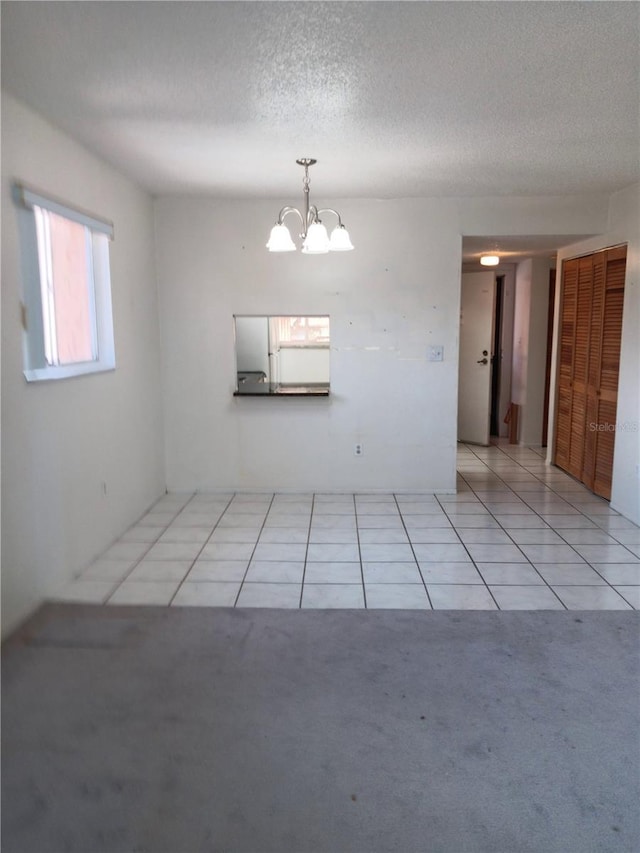 empty room with light colored carpet, a notable chandelier, a textured ceiling, and light tile patterned floors