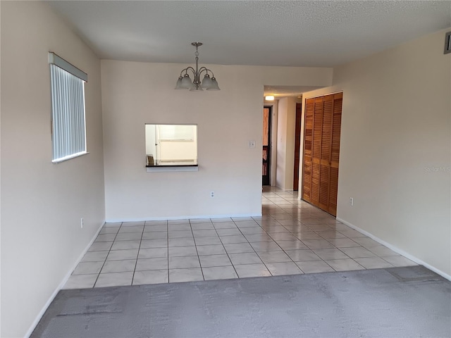 spare room featuring a textured ceiling, light tile patterned flooring, visible vents, baseboards, and an inviting chandelier