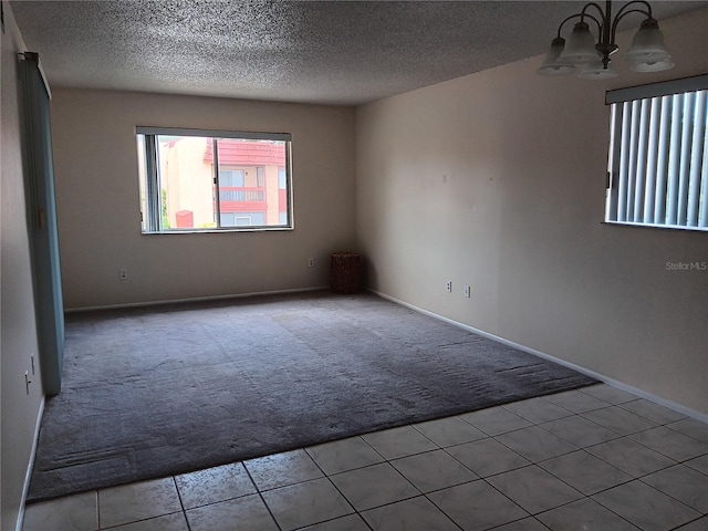 empty room featuring an inviting chandelier, baseboards, a textured ceiling, and light colored carpet