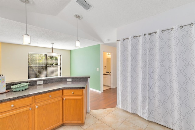 kitchen featuring hanging light fixtures, a textured ceiling, vaulted ceiling, and light hardwood / wood-style flooring