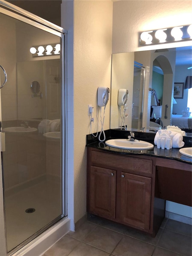 bathroom with tile flooring, a shower with shower door, and dual bowl vanity