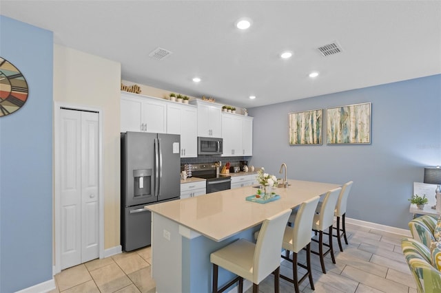 kitchen featuring backsplash, appliances with stainless steel finishes, a breakfast bar, light tile floors, and a center island with sink