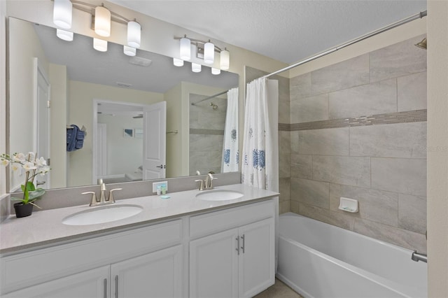 bathroom featuring large vanity, dual sinks, shower / bathtub combination with curtain, and a textured ceiling