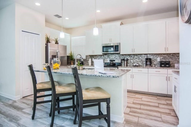 kitchen featuring an island with sink, pendant lighting, backsplash, stainless steel appliances, and white cabinetry