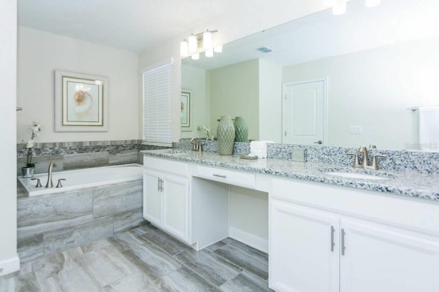 bathroom with tiled tub and dual bowl vanity