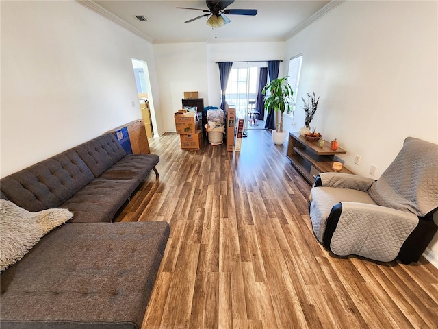 living room with ornamental molding, a ceiling fan, visible vents, and wood finished floors