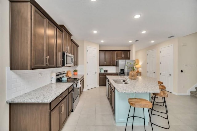 kitchen with light tile floors, light stone countertops, a kitchen island with sink, and stainless steel appliances