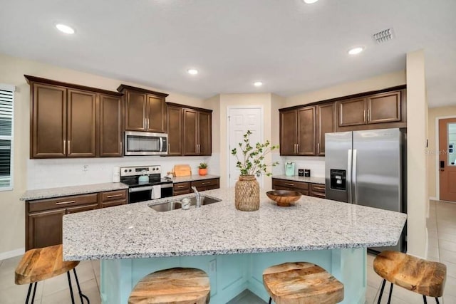 kitchen featuring a breakfast bar, a kitchen island with sink, appliances with stainless steel finishes, and light stone counters