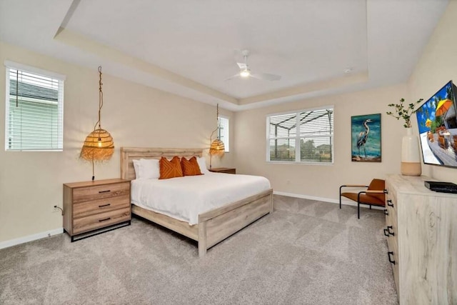 carpeted bedroom featuring a raised ceiling, ceiling fan, and multiple windows