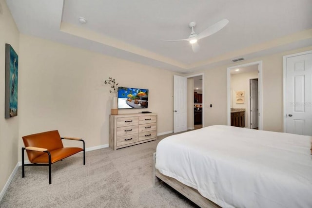 bedroom with a raised ceiling, ensuite bath, light colored carpet, and ceiling fan