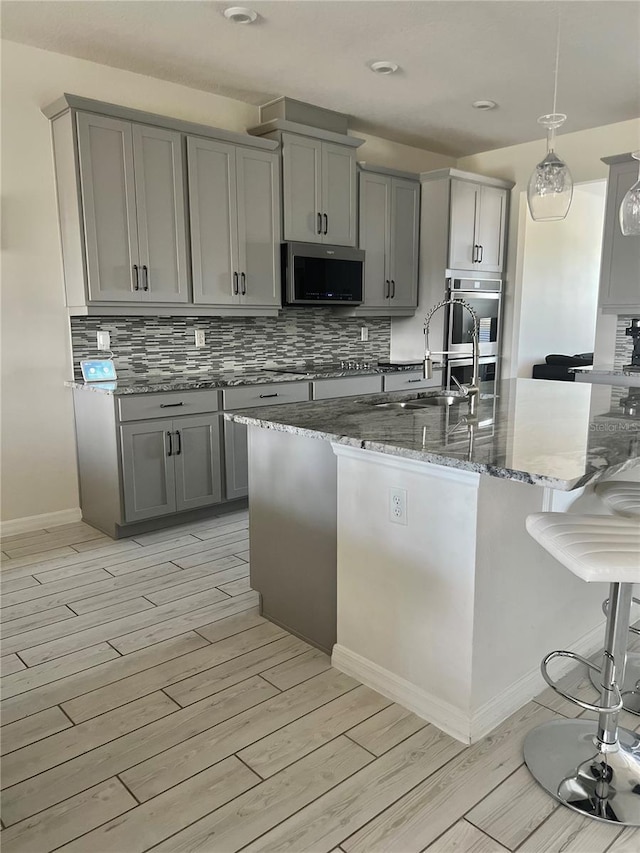 kitchen with gray cabinets, appliances with stainless steel finishes, pendant lighting, dark stone counters, and light hardwood / wood-style floors