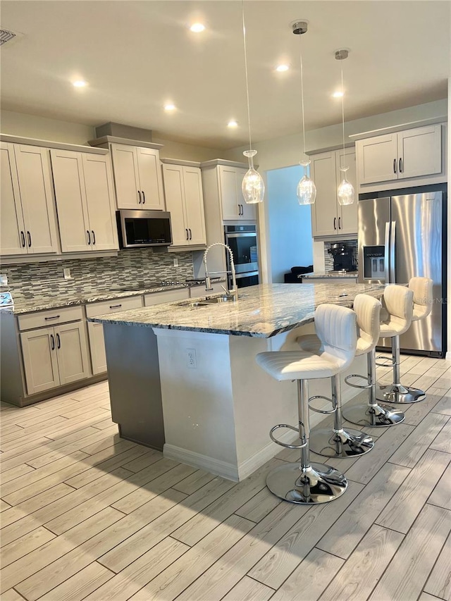 kitchen featuring decorative light fixtures, sink, a kitchen island with sink, stainless steel appliances, and light stone countertops