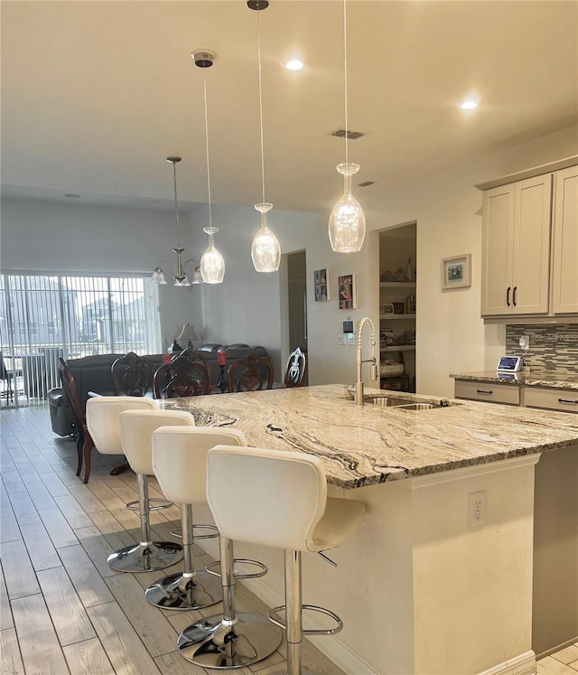 kitchen featuring a breakfast bar area, pendant lighting, a large island, light hardwood / wood-style floors, and backsplash