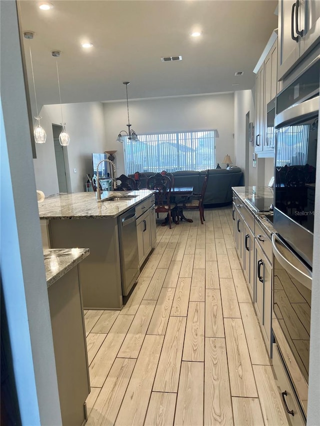 kitchen featuring appliances with stainless steel finishes, decorative light fixtures, sink, gray cabinetry, and a kitchen island with sink