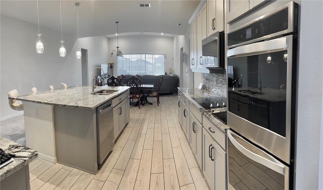 kitchen featuring pendant lighting, sink, appliances with stainless steel finishes, gray cabinetry, and a center island with sink