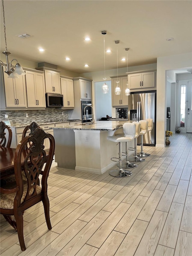 kitchen with pendant lighting, appliances with stainless steel finishes, and a kitchen island with sink