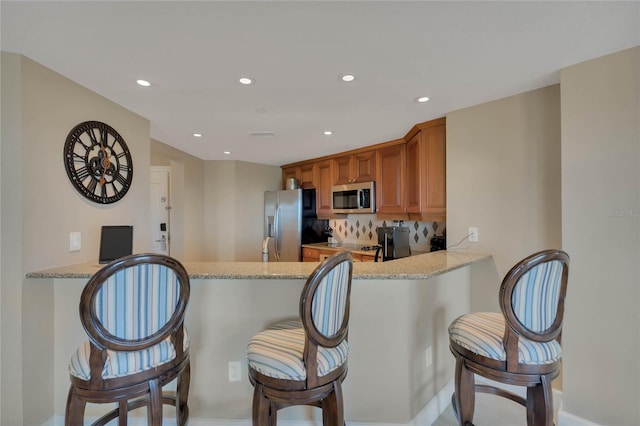 kitchen with kitchen peninsula, a breakfast bar, stainless steel appliances, light stone countertops, and tasteful backsplash