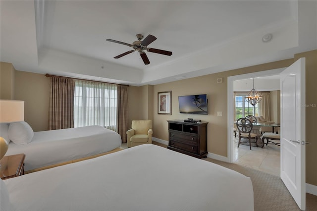 tiled bedroom featuring ceiling fan with notable chandelier and a tray ceiling