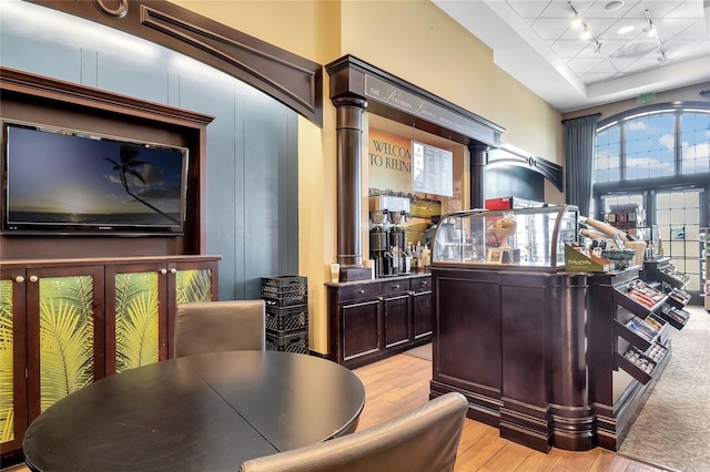 bar with a towering ceiling, dark brown cabinets, light hardwood / wood-style floors, decorative columns, and a tray ceiling