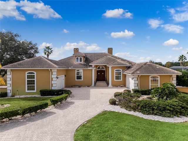 mediterranean / spanish house featuring decorative driveway, an attached garage, a chimney, and a tiled roof