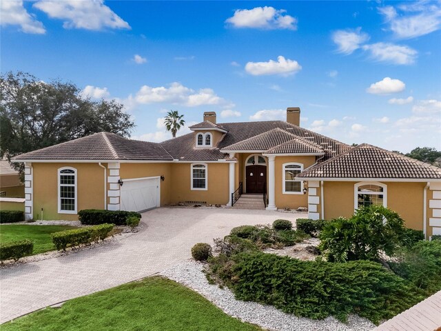 mediterranean / spanish-style house featuring stucco siding, driveway, an attached garage, and a tiled roof