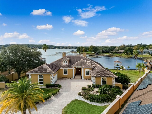 view of front of home featuring fence, driveway, stucco siding, a water view, and a tiled roof