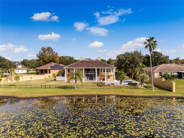 rear view of house with a chimney, fence private yard, a yard, and a water view