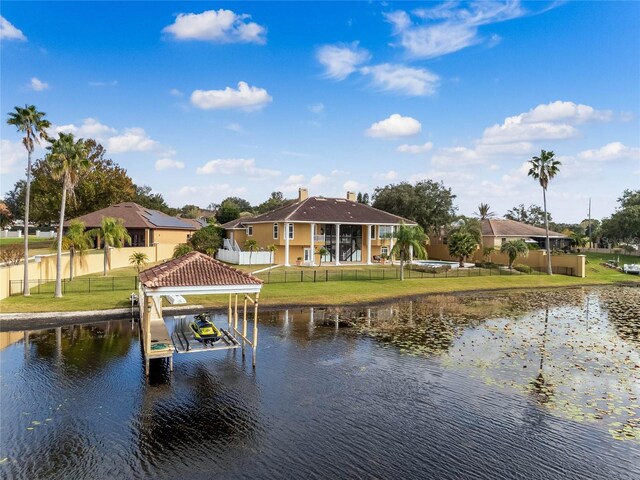 view of dock with a yard, fence, a water view, and boat lift