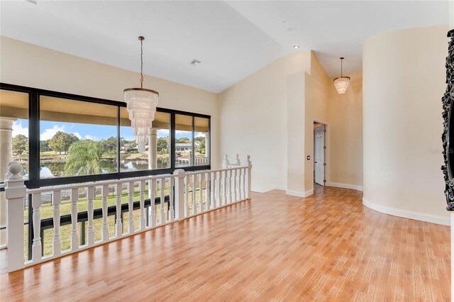 empty room featuring wood finished floors, visible vents, baseboards, high vaulted ceiling, and a notable chandelier