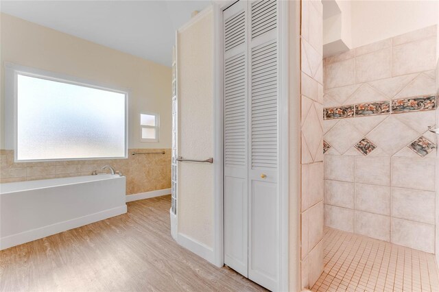 full bathroom featuring wood finished floors, a tile shower, a closet, baseboards, and a bath