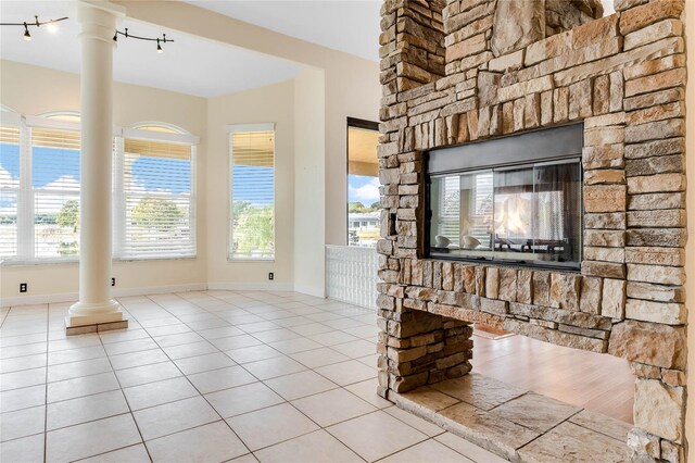 unfurnished living room with tile patterned flooring, a fireplace, baseboards, and ornate columns