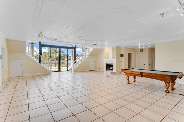 rec room featuring light tile patterned floors, visible vents, a lit fireplace, and rail lighting