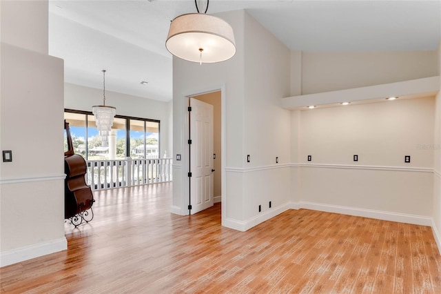 empty room with an inviting chandelier, light wood-style flooring, baseboards, and high vaulted ceiling