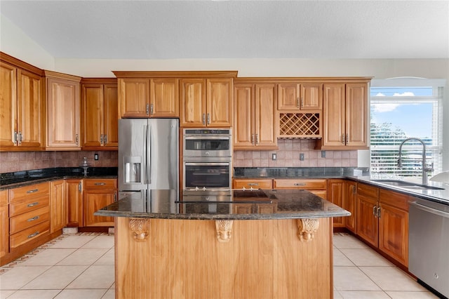 kitchen featuring light tile patterned floors, a sink, appliances with stainless steel finishes, backsplash, and a center island