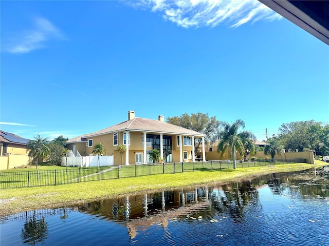 back of house featuring fence, a yard, a chimney, stucco siding, and a water view