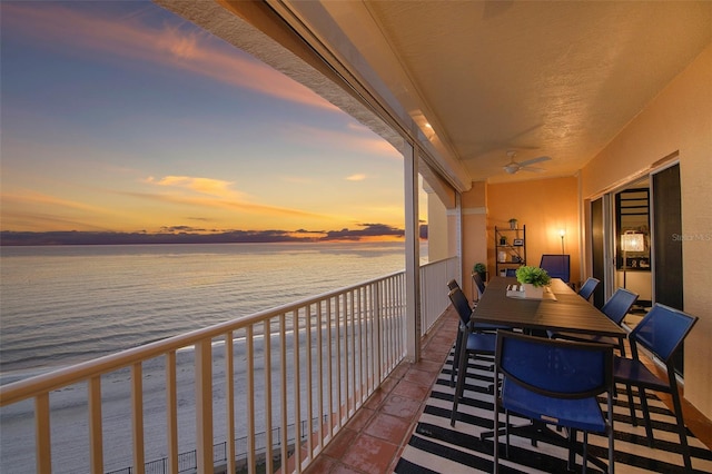 balcony at dusk with a water view and ceiling fan