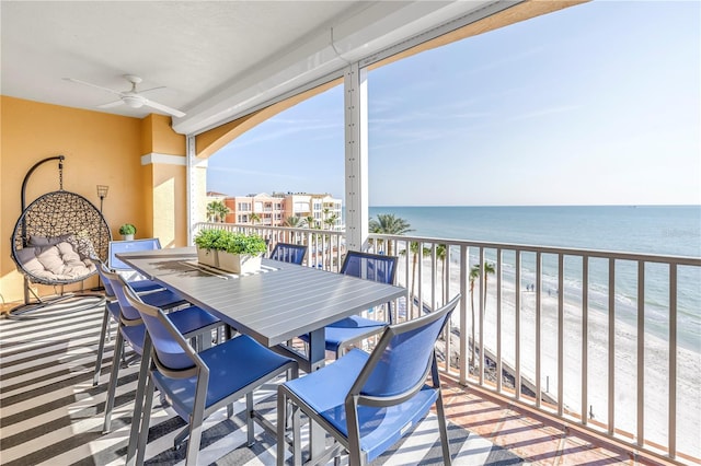 balcony featuring a ceiling fan, outdoor dining area, a water view, and a beach view