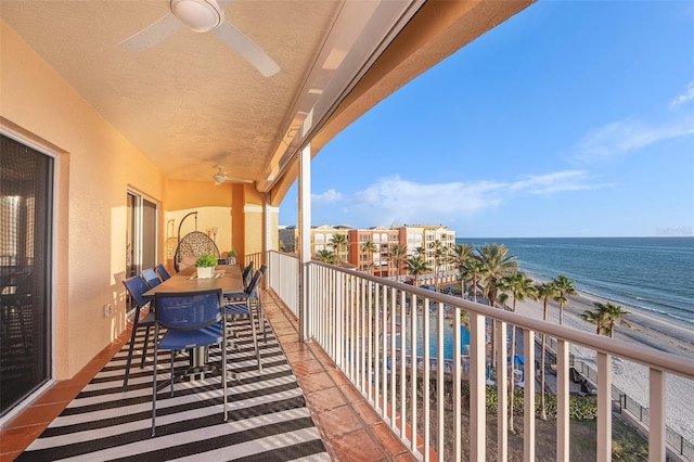 balcony featuring a beach view, a water view, and a ceiling fan