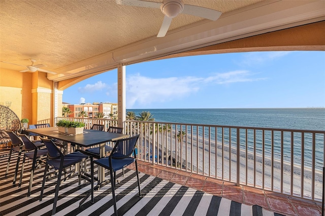 balcony featuring outdoor dining area, a water view, ceiling fan, and a beach view