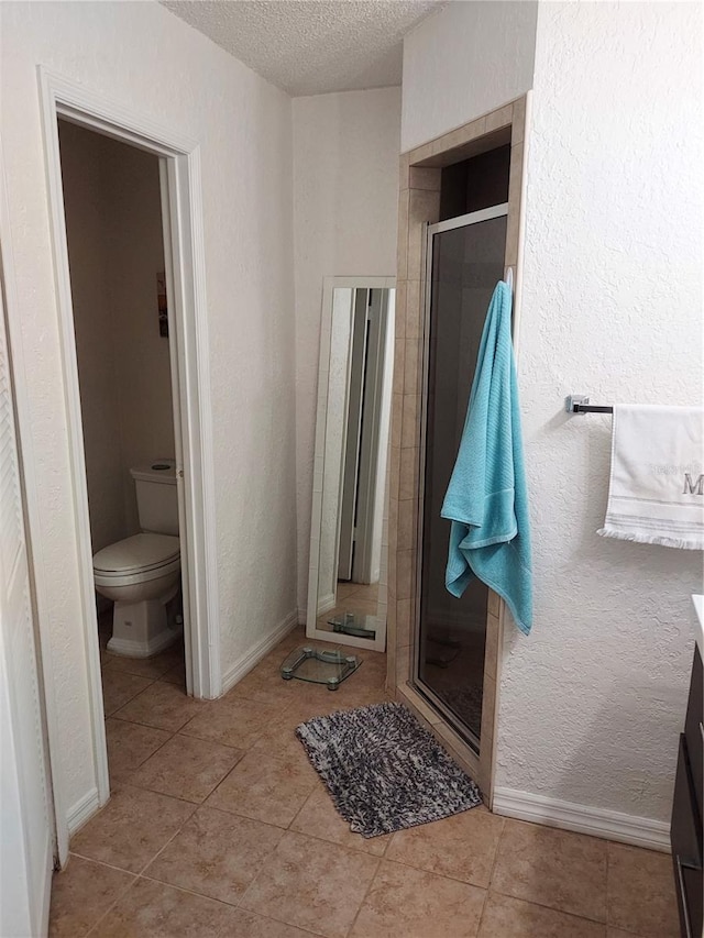 bathroom with vanity, tile floors, a shower with door, a textured ceiling, and toilet