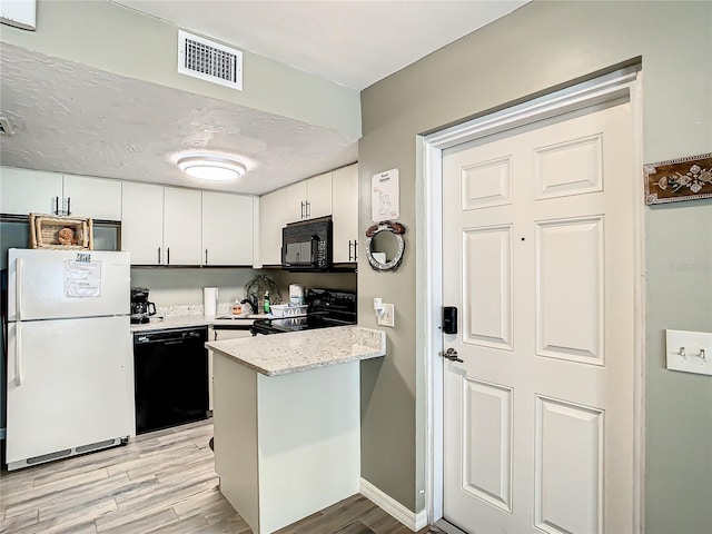 kitchen with light wood-type flooring, light stone countertops, black appliances, and white cabinetry