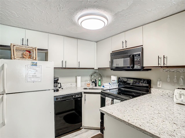 kitchen with white cabinetry, light stone counters, black appliances, and sink